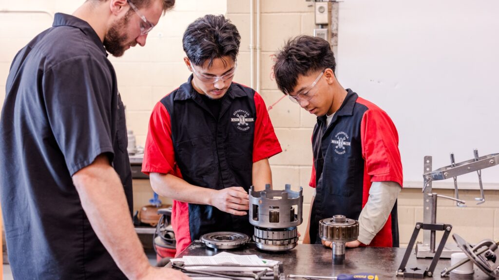 Two automotive students and instructor working on parts in class.